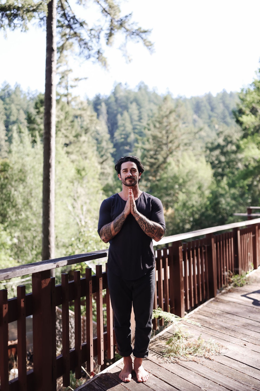 Peter standing in prayer hands on a forest deck, all-black, contemplative.